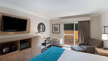 A hotel room with a bed, a desk with a chair, a television, a microwave, a large window with curtains, and a balcony with a table and chairs.