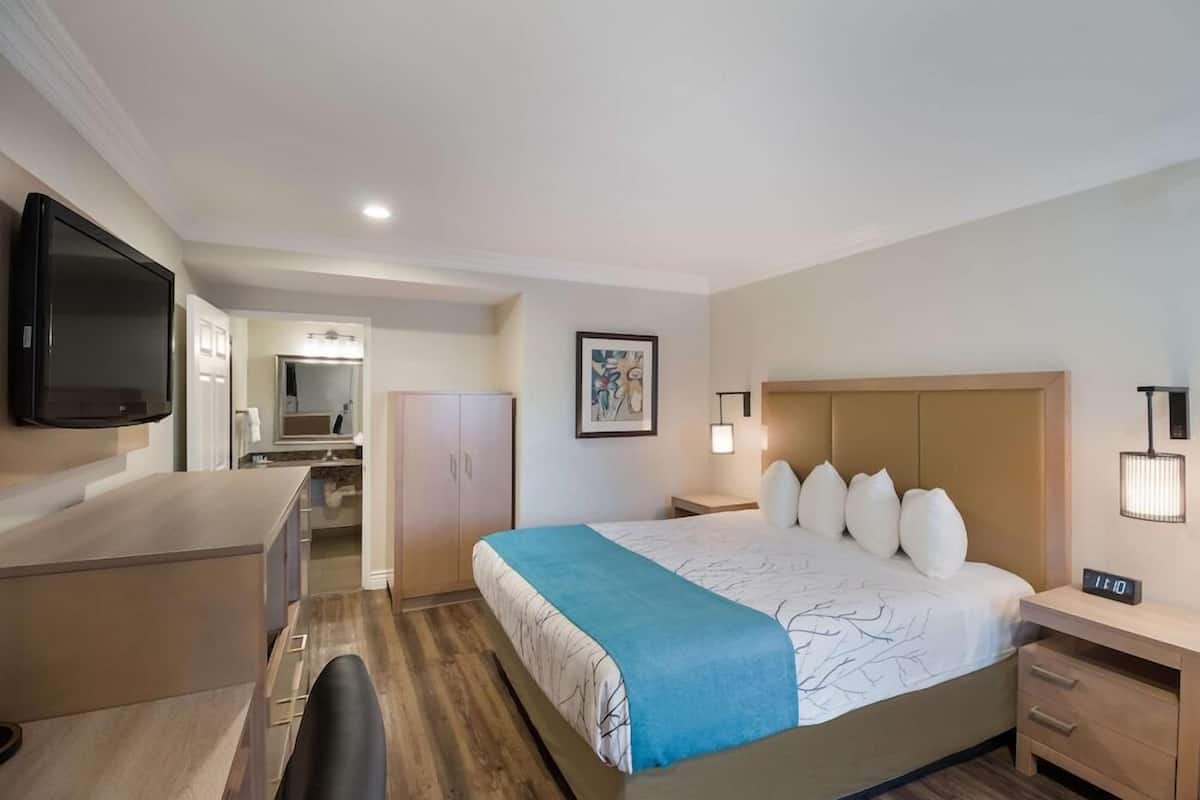 A hotel room with a bed, bedside table, TV, and a kitchenette area.