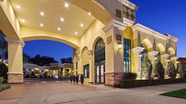 Entrada de hotel con un vestíbulo cubierto, ventanas en arco y fachada de piedra.
