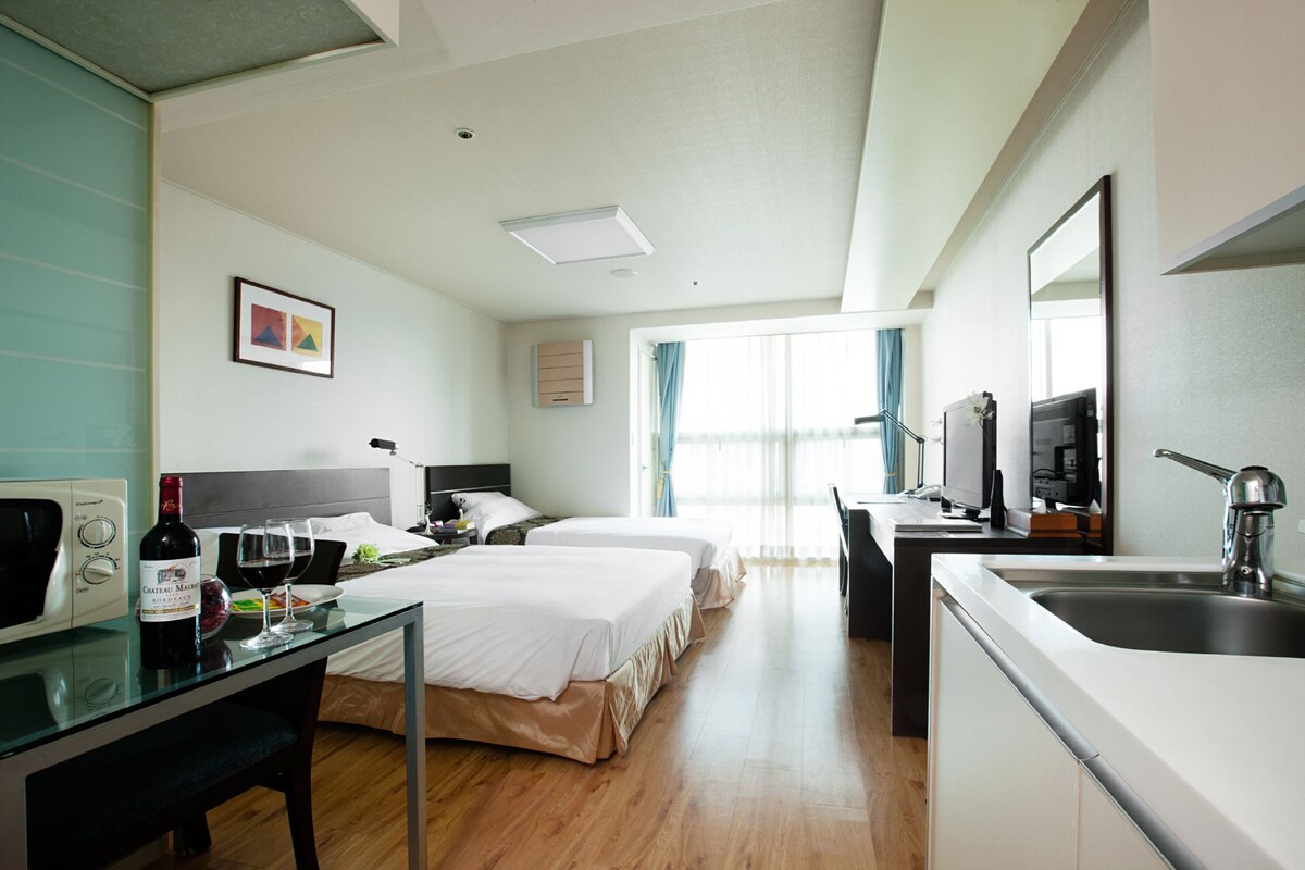 A hotel room with two beds, a desk with a computer, a sink, and a television.