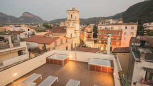 Terraza en la azotea con sillones de sol y un jacuzzi, con vistas a un pueblo con edificios históricos y una torre destacada.