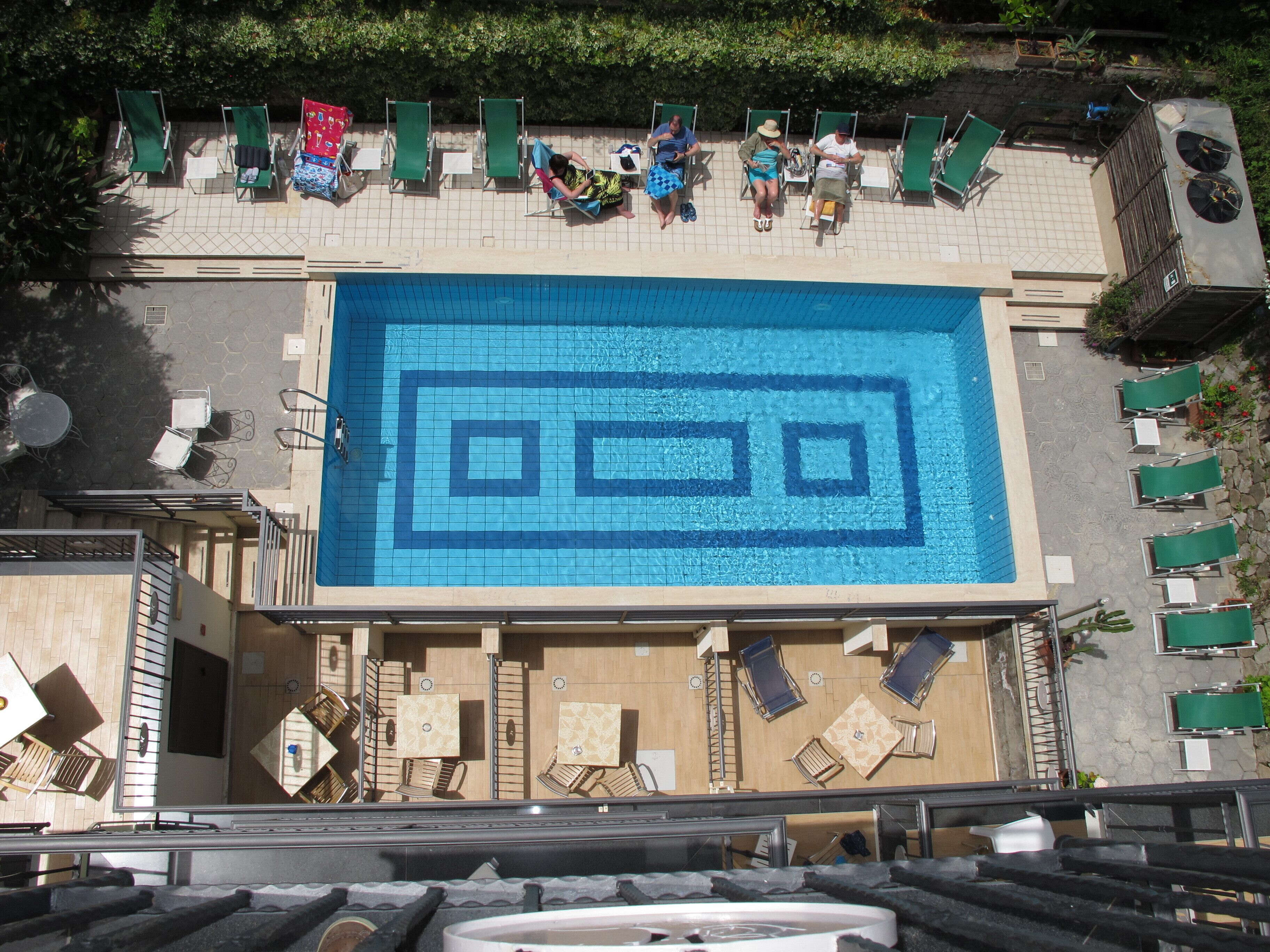 Piscina no terraço com padrão geométrico de azulejos, cercada por espreguiçadeiras e mesas.