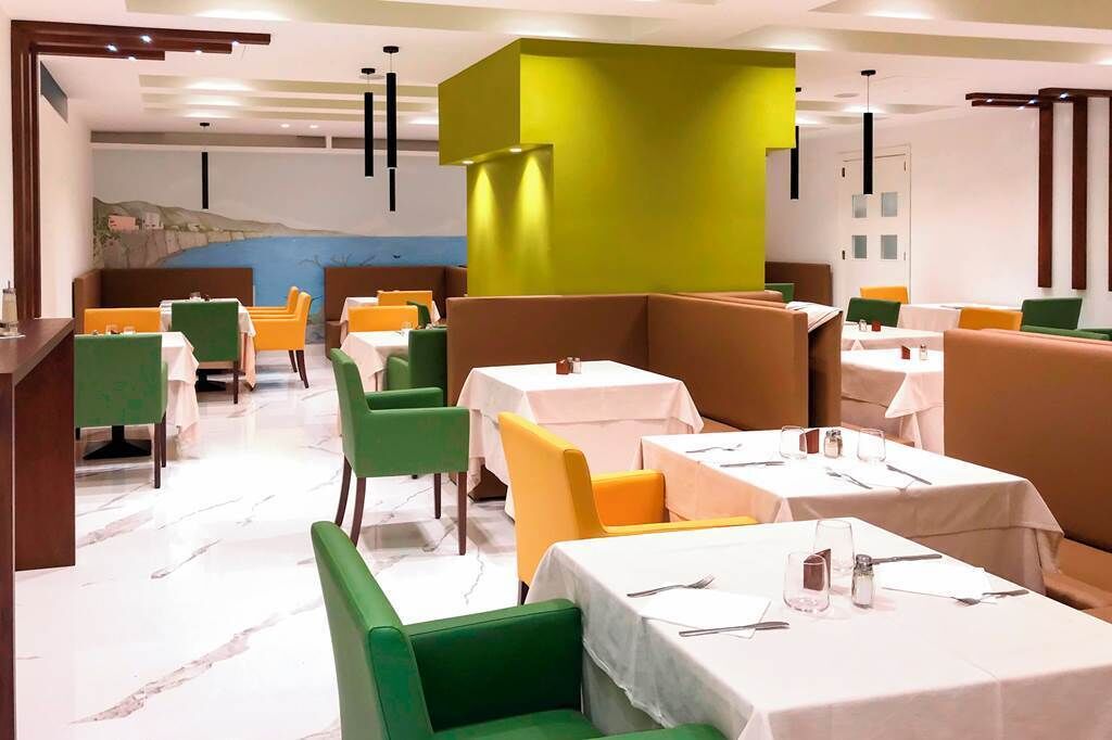 A restaurant with booths and tables, some with green and yellow chairs, and a mural on the wall.