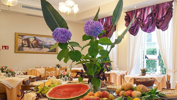 Comedor con mesas dispuestas para una comida, con una variedad de frutas y una sandía grande como centro de mesa.