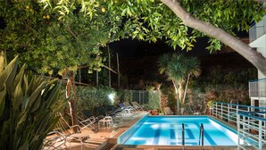Una piscina al aire libre con sillones de descanso y un muro de piedra al fondo.