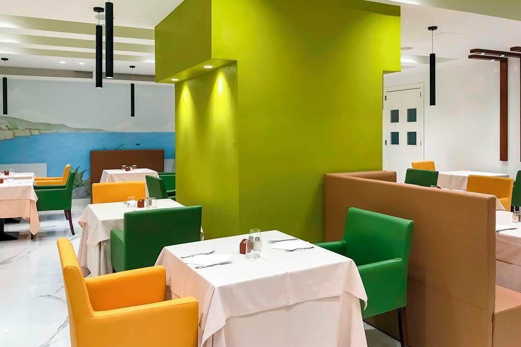 Un restaurante con cabinas y mesas, asientos verdes y anaranjados, y un mural en la pared.