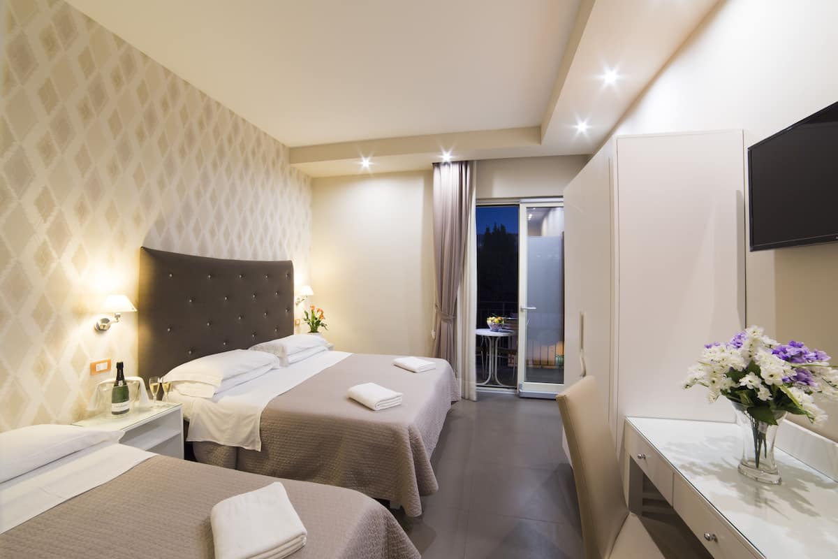 Ein Hotelzimmer mit zwei Betten, einer Minibar, einem Fernseher und einem Badezimmer mit Spiegel und Waschbecken.