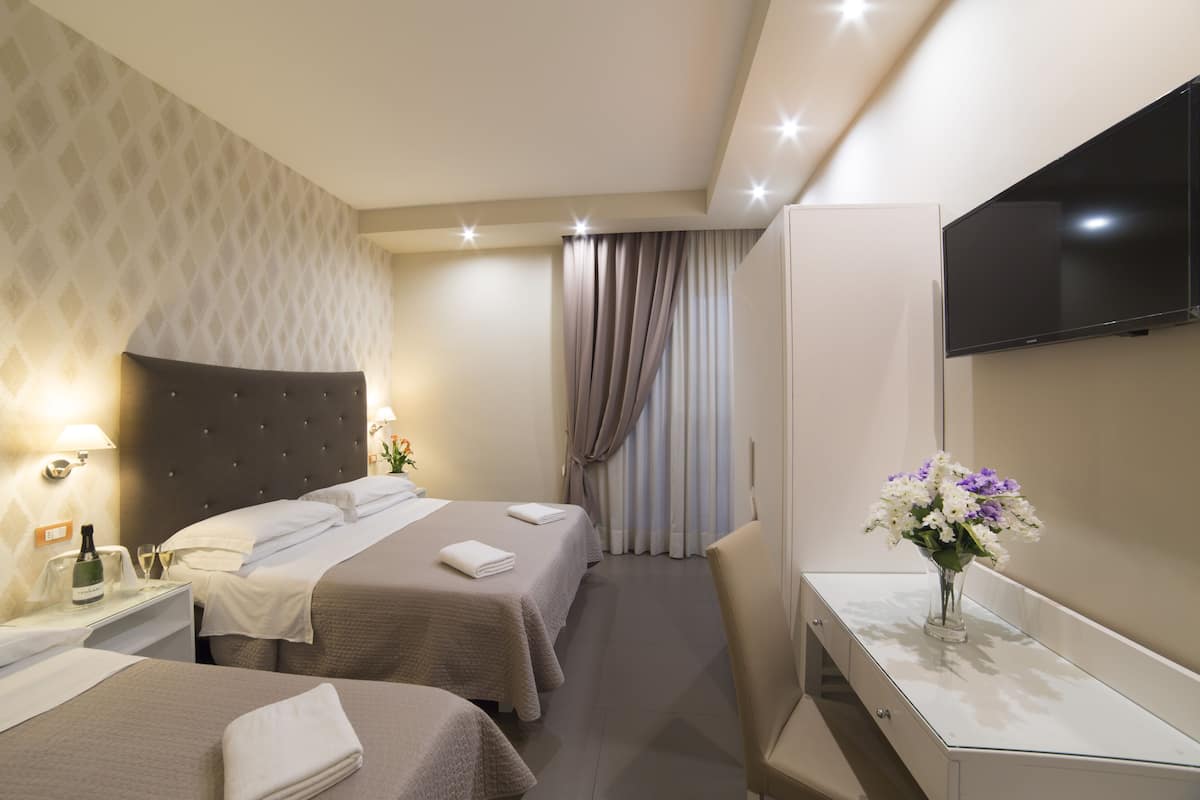 Ein Hotelzimmer mit zwei Betten, einem Schreibtisch, einem Fernseher und einer Blumenvase.