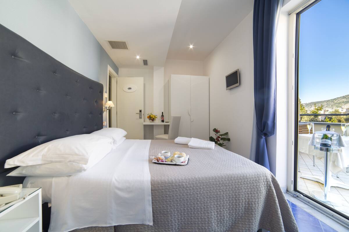 Ein Hotelzimmer mit einem großen Bett, einem Nachttisch, einem Fenster mit Blick nach außen und einem durchgehenden Türspalt sichtbaren Badezimmer.