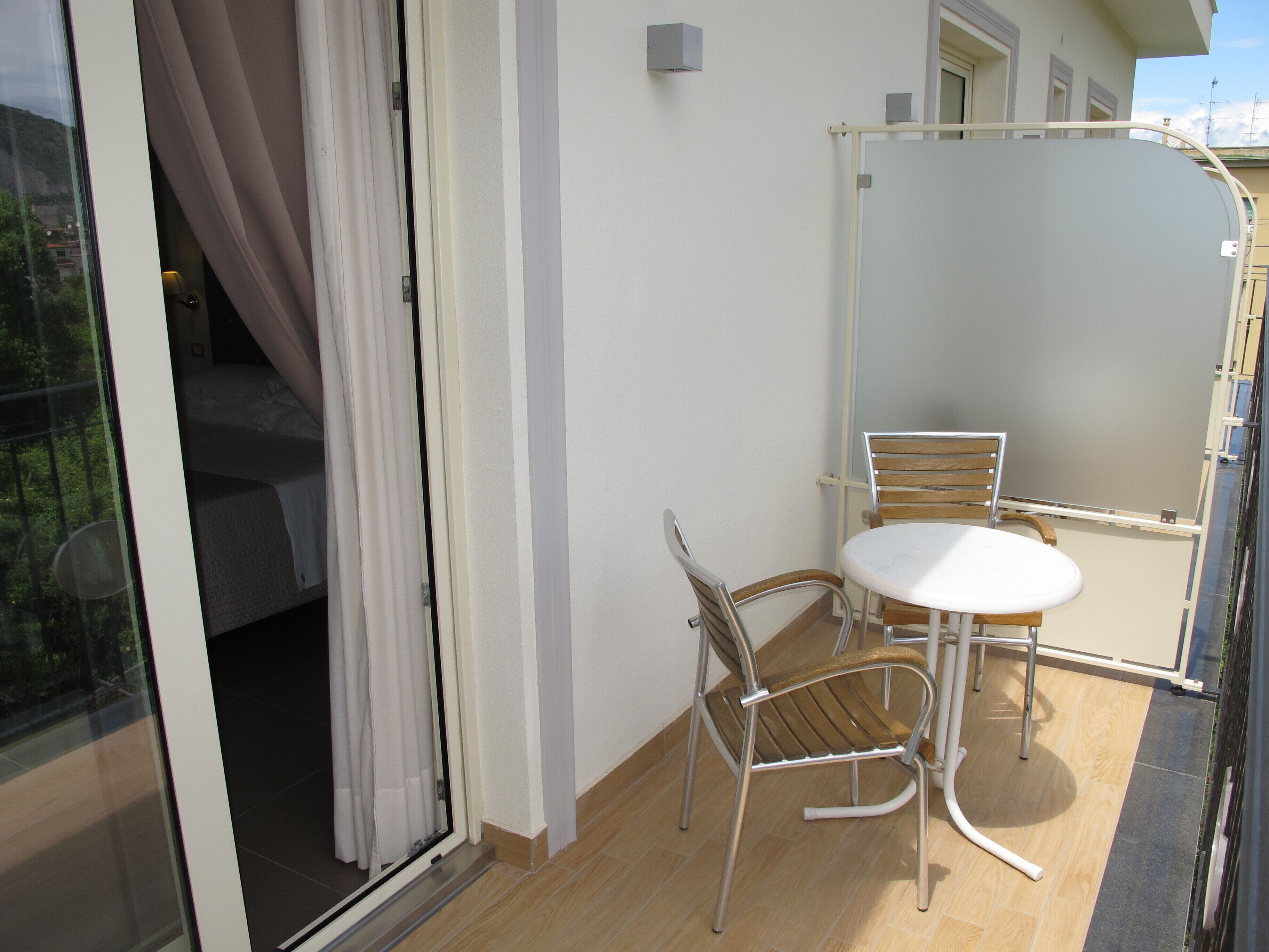 A balcony with a glass door, a small table, two chairs, and a view of a building.