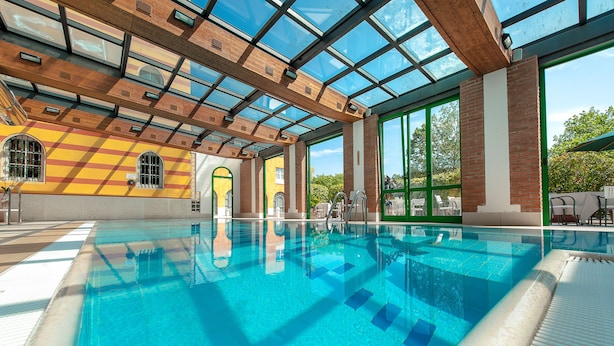 A swimming pool with clear blue water, surrounded by large windows and a glass ceiling. - Hotel Villa Malaspina (Castel d'Azzano)