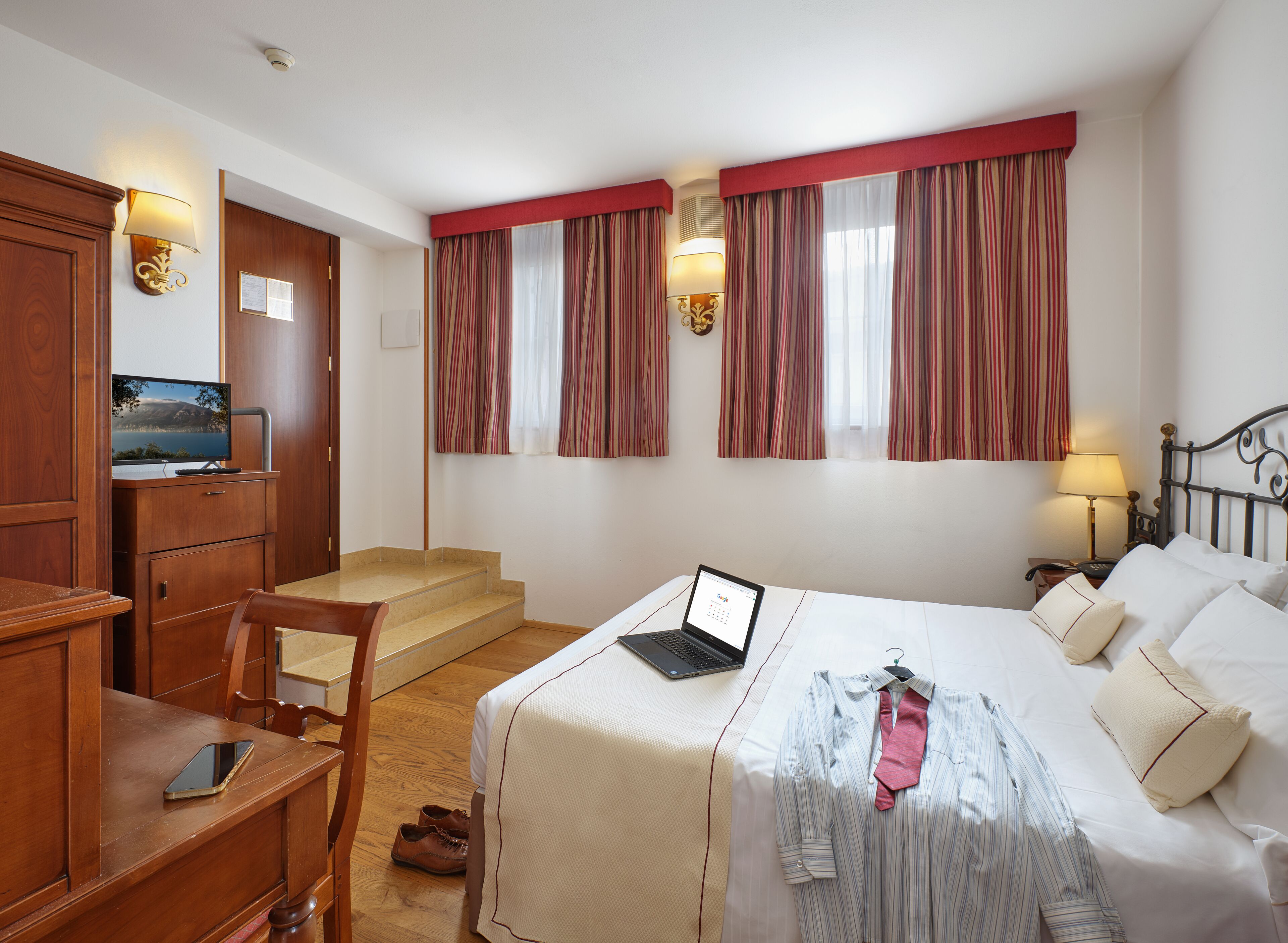 A hotel room with a bed, a desk, a chair, a TV, and a window with curtains.