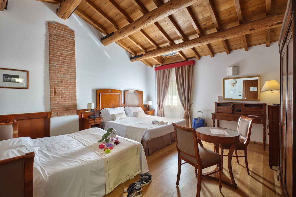 Une chambre d’hôtel avec deux lits, un bureau, une chaise, une valise et un miroir.