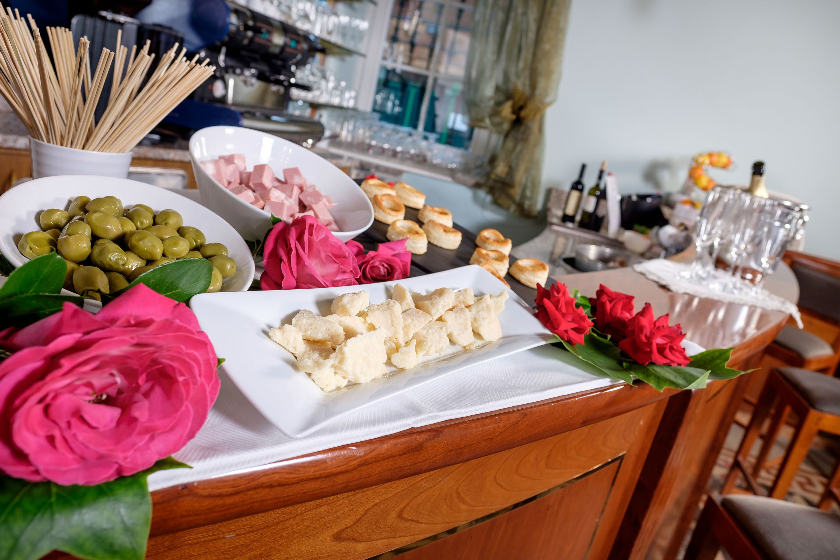 Ein reichhaltiges Buffet mit verschiedenen Speisen, darunter Oliven, Schinken und Gebäck, sowie ein Strauß roter Rosen.