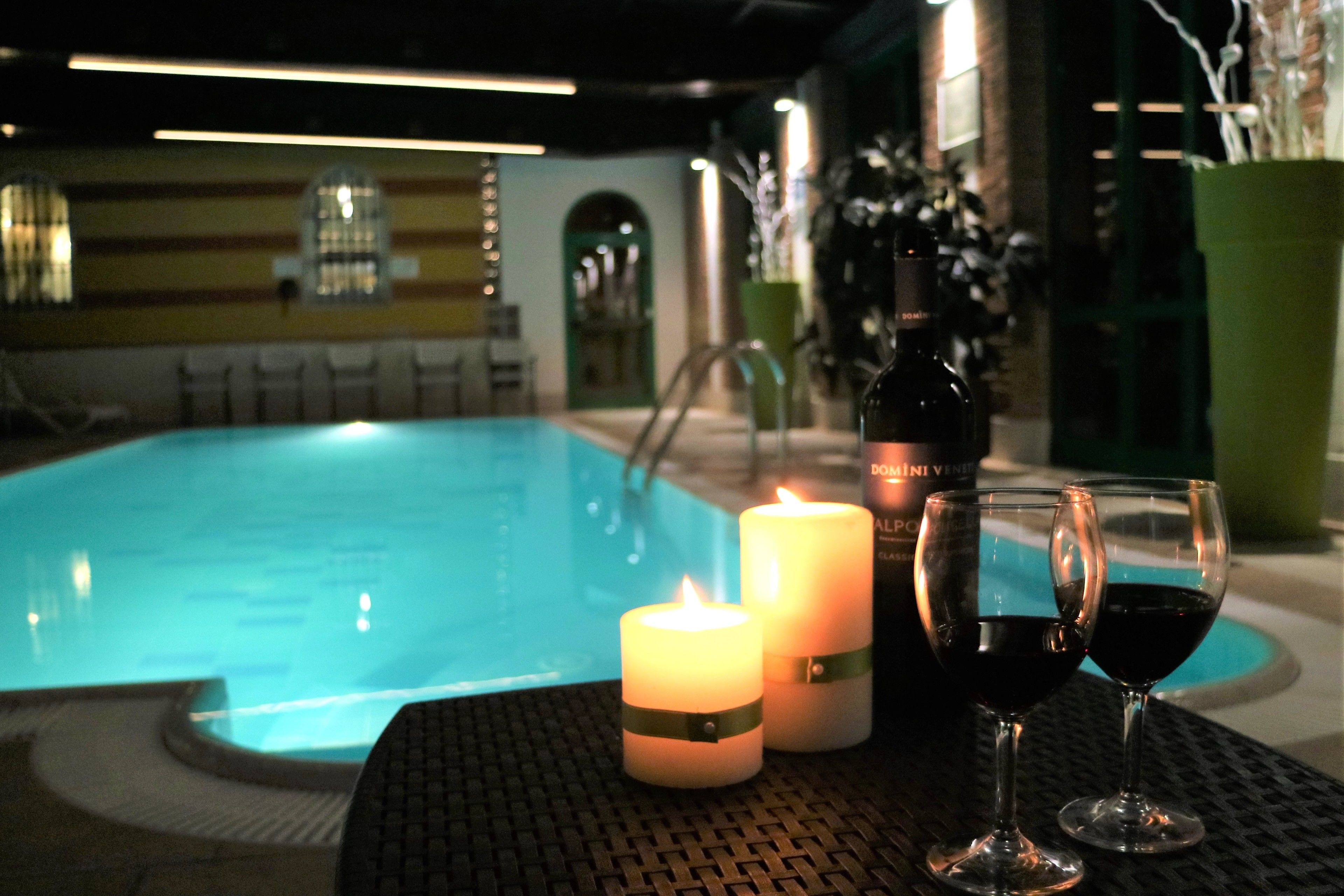 A poolside setting with a pool, candles, and wine glasses.