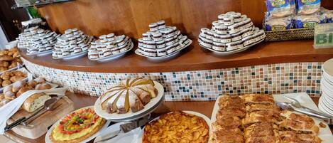 A buffet with various food items including pastries, cakes, and a variety of breads.