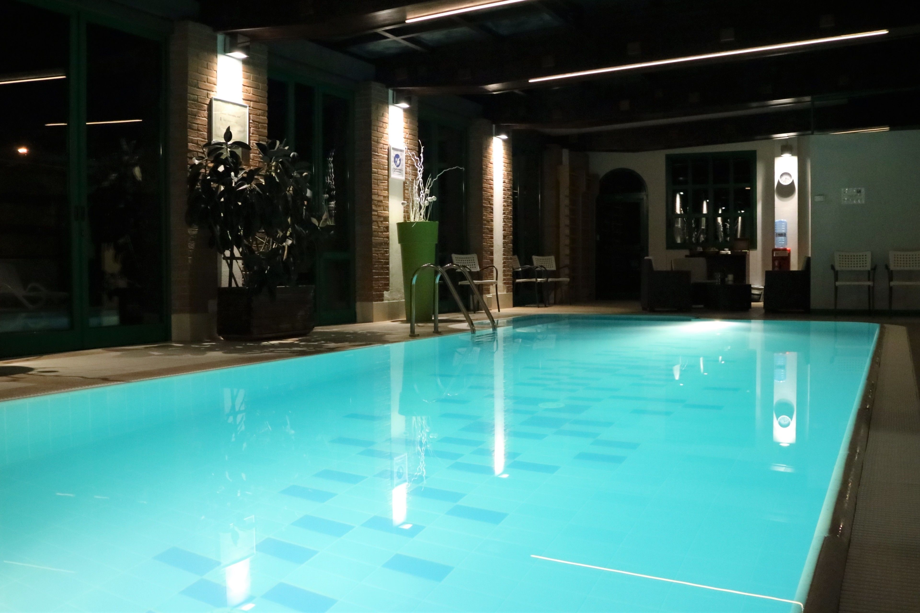 An indoor swimming pool with clear blue water, surrounded by brick walls and potted plants.