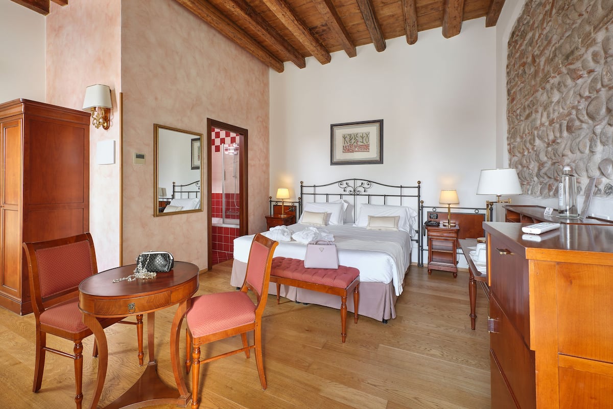 Une chambre d’hôtel avec un plafond en bois, un lit avec du linge de maison blanc, un bureau avec une lampe et une chaise.