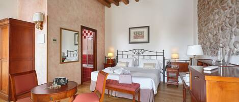 A hotel room with a wooden ceiling, a bed with white linens, a desk with a lamp, and a chair.