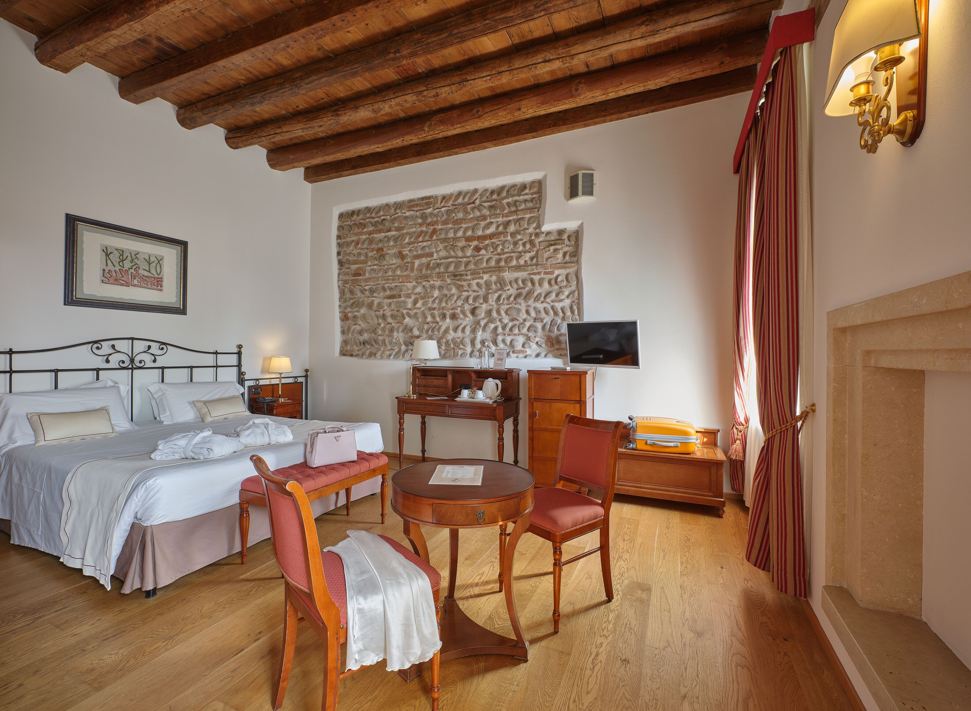 A hotel room with a bed, a desk, a chair, a television, and a stone wall.