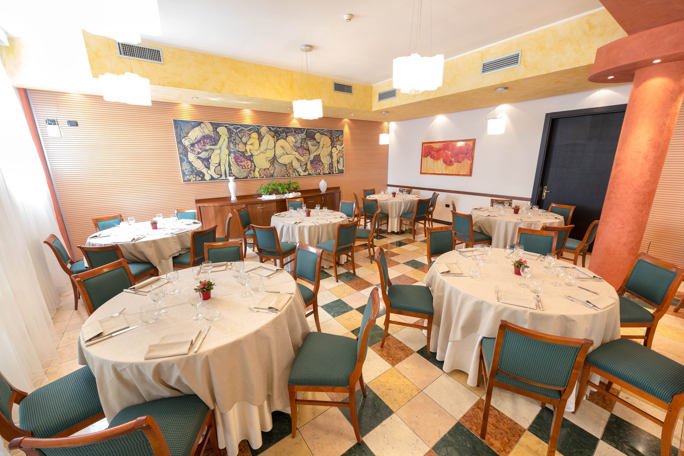 A dining area with multiple round tables, green upholstered chairs, and a checkered floor pattern.
