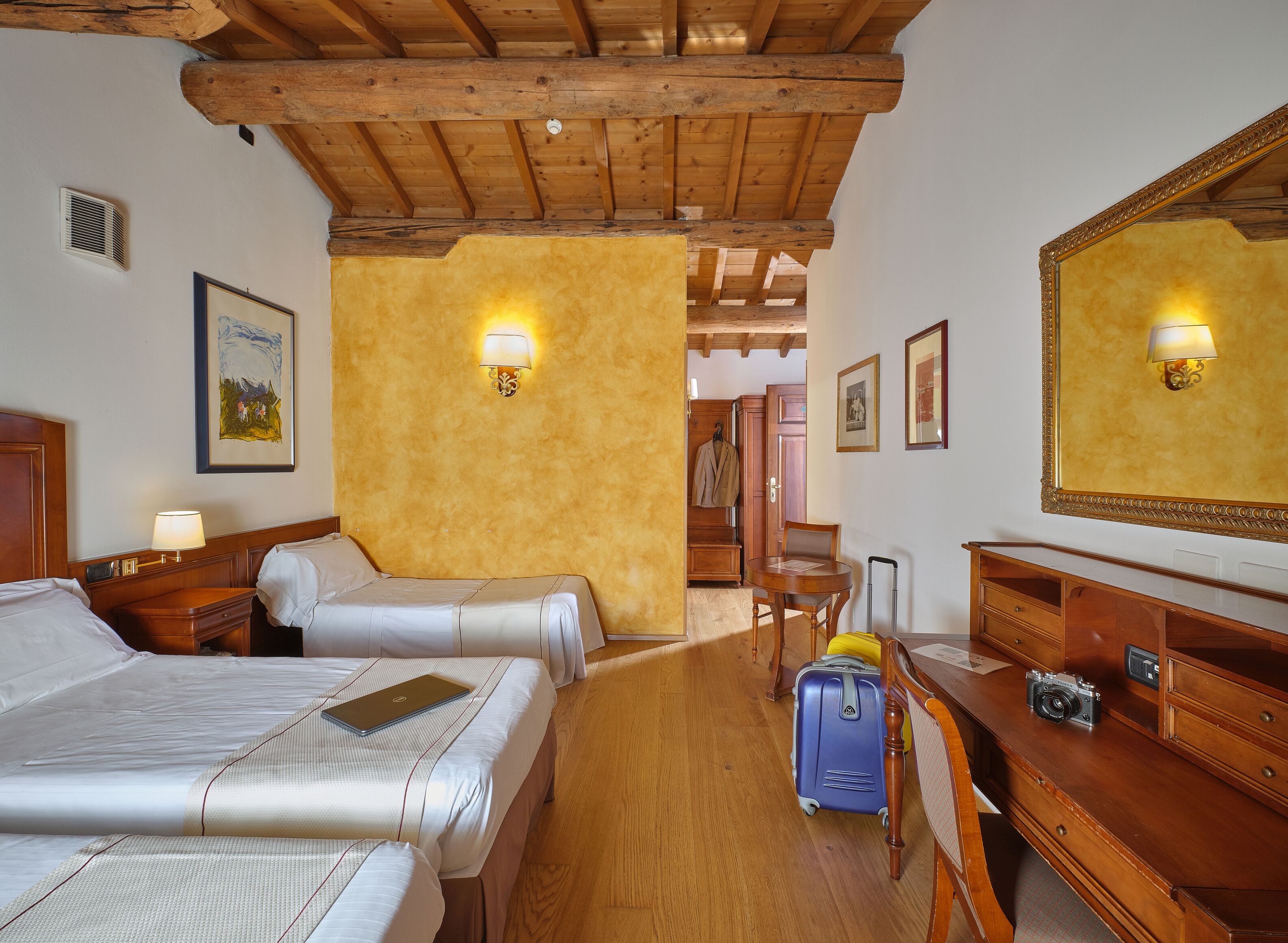 A hotel room with two beds, a wooden desk, a chair, a suitcase, and a camera.