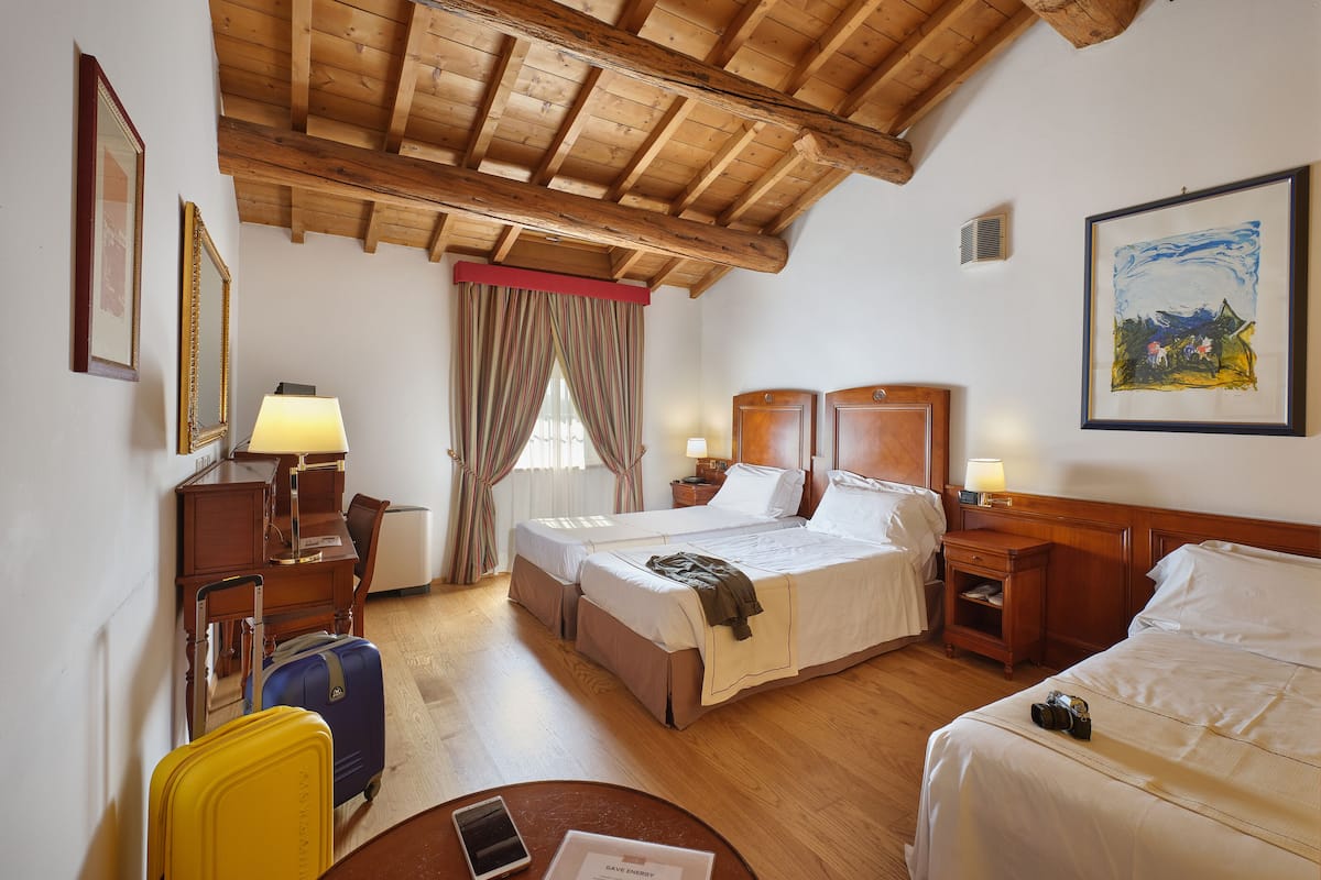 Une chambre d’hôtel avec deux lits, des poutres apparentes en bois au plafond, un tableau et un bureau avec une lampe.