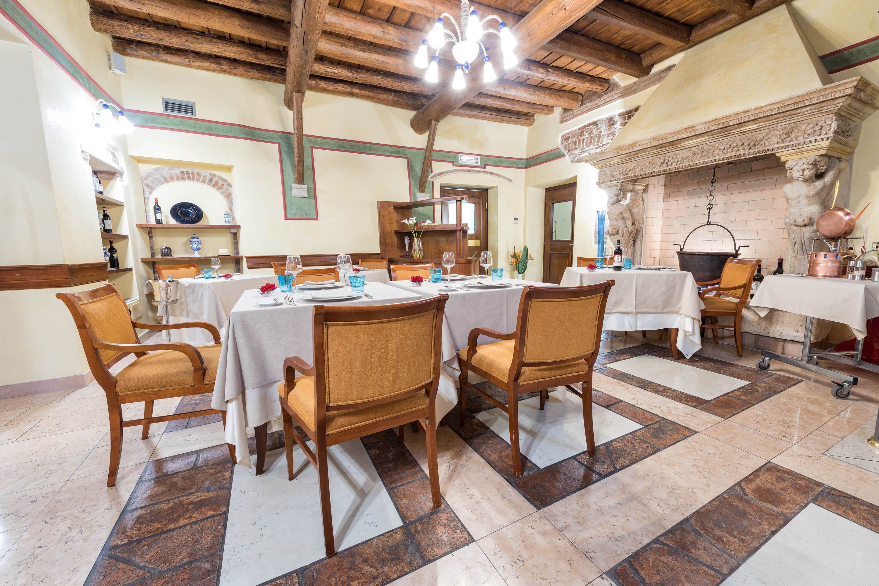 A dining area with wooden chairs and tables, a tiled floor, and a fireplace with decorative elements.