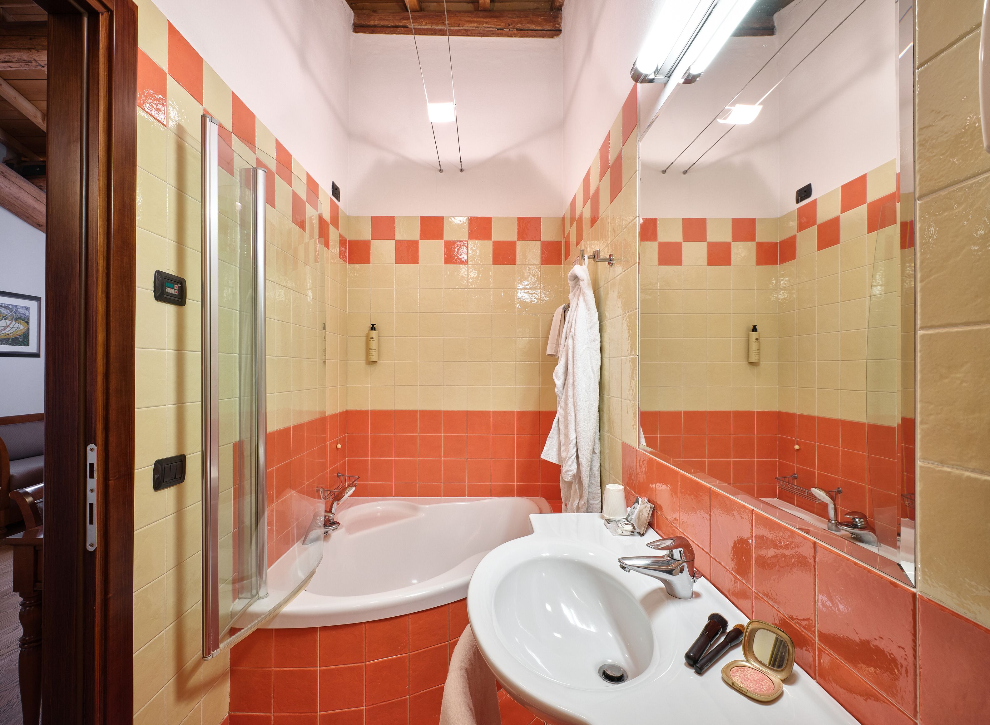 A bathroom with a bathtub, a sink, and a mirror. There are orange and beige tiles on the walls.