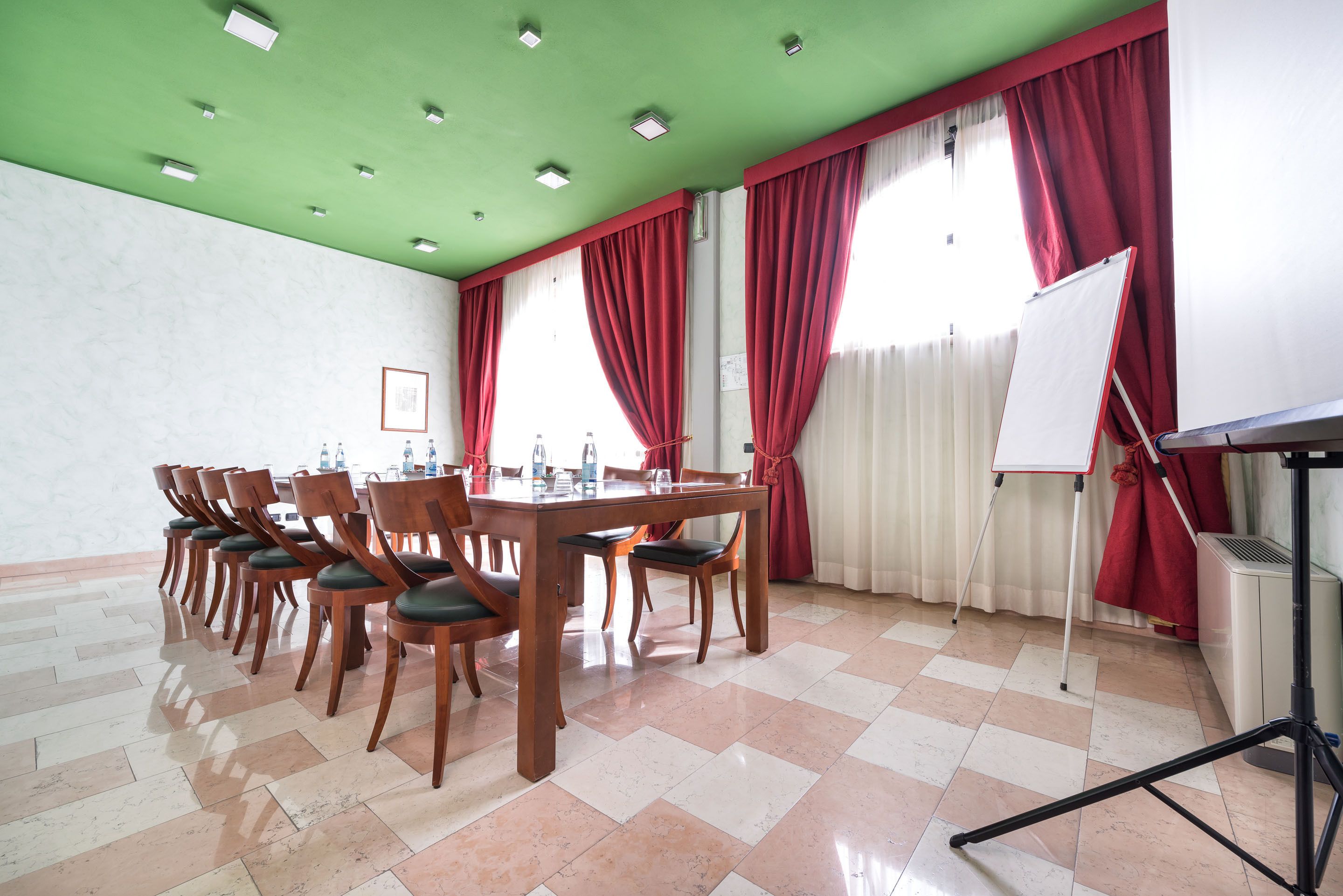 A conference room with a green ceiling, red curtains, a whiteboard on a stand, and a tiled floor.