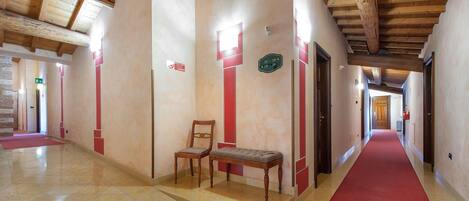 Um corredor de hotel com carpete vermelho, bancos de madeira e piso ladrilhado.