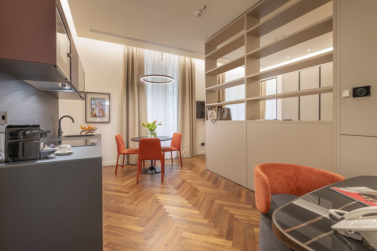 Eine moderne Küche mit integrierter Espressomaschine, ein Essbereich mit rundem Tisch und orangefarbenen Stühlen sowie ein großes Fenster mit Vorhängen.