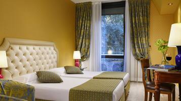 Ein Hotelzimmer mit einem großen Bett, zwei Nachttischen, einem Schreibtisch mit Stuhl und einem fensterbepflanzten Fenster.