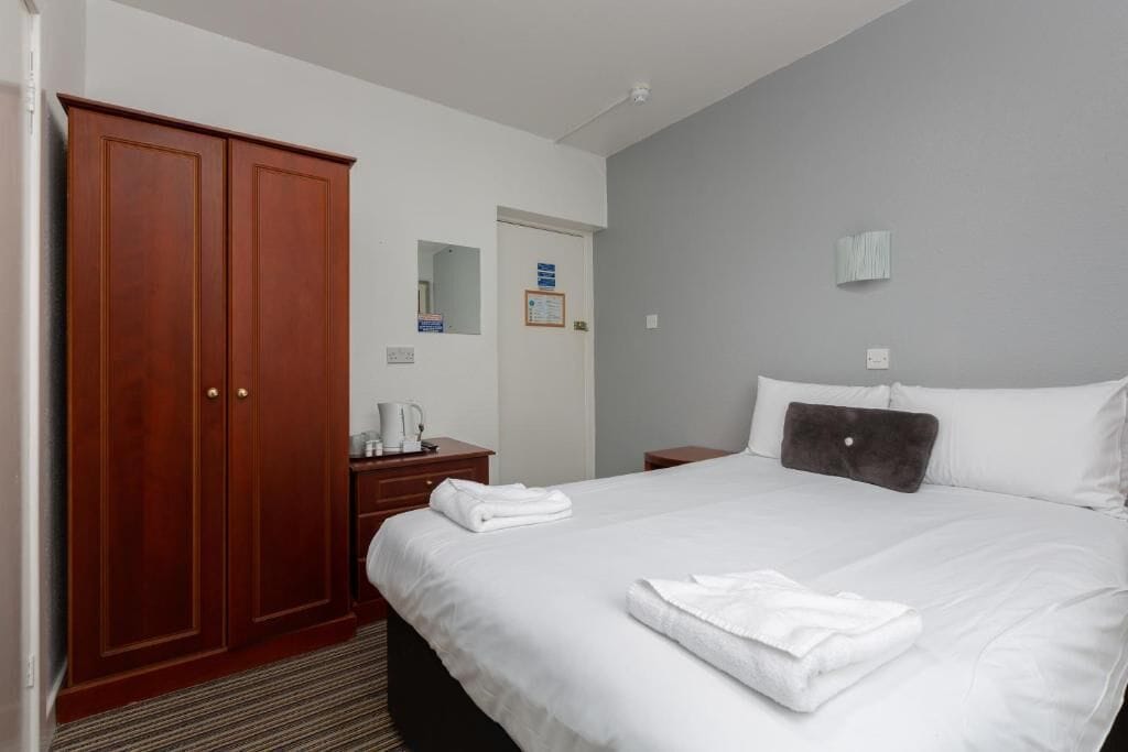 A hotel room with a large bed, a wardrobe, a desk with a lamp, and a mirror.
