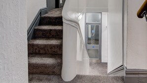 Una escalera con moqueta, barandilla, una puerta y un pequeño ventanal.