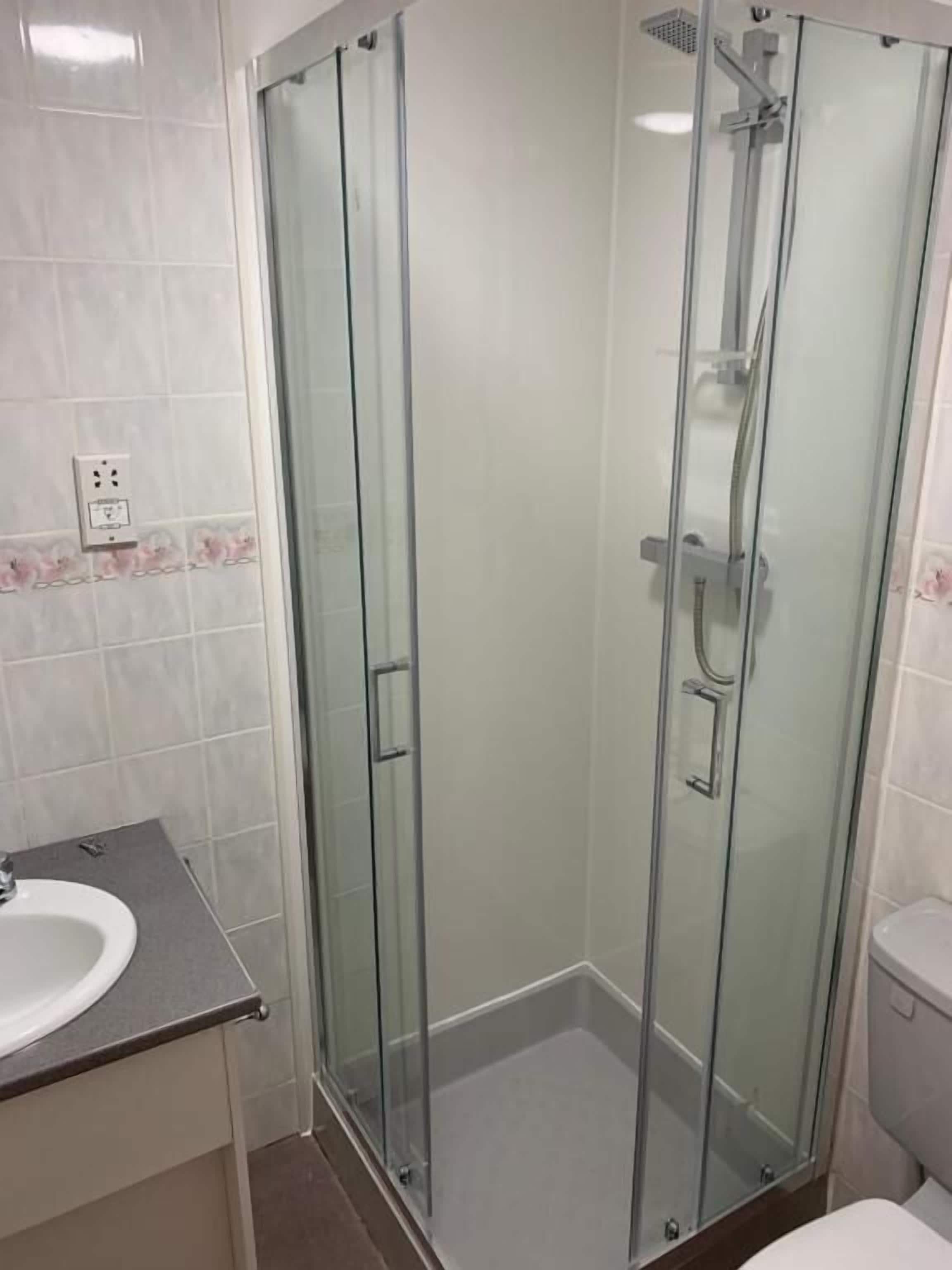 A glass-enclosed shower with a handheld showerhead and a wall-mounted faucet.