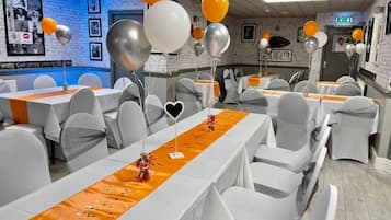 A banquet hall with tables set for events, featuring white chairs and orange table runners.