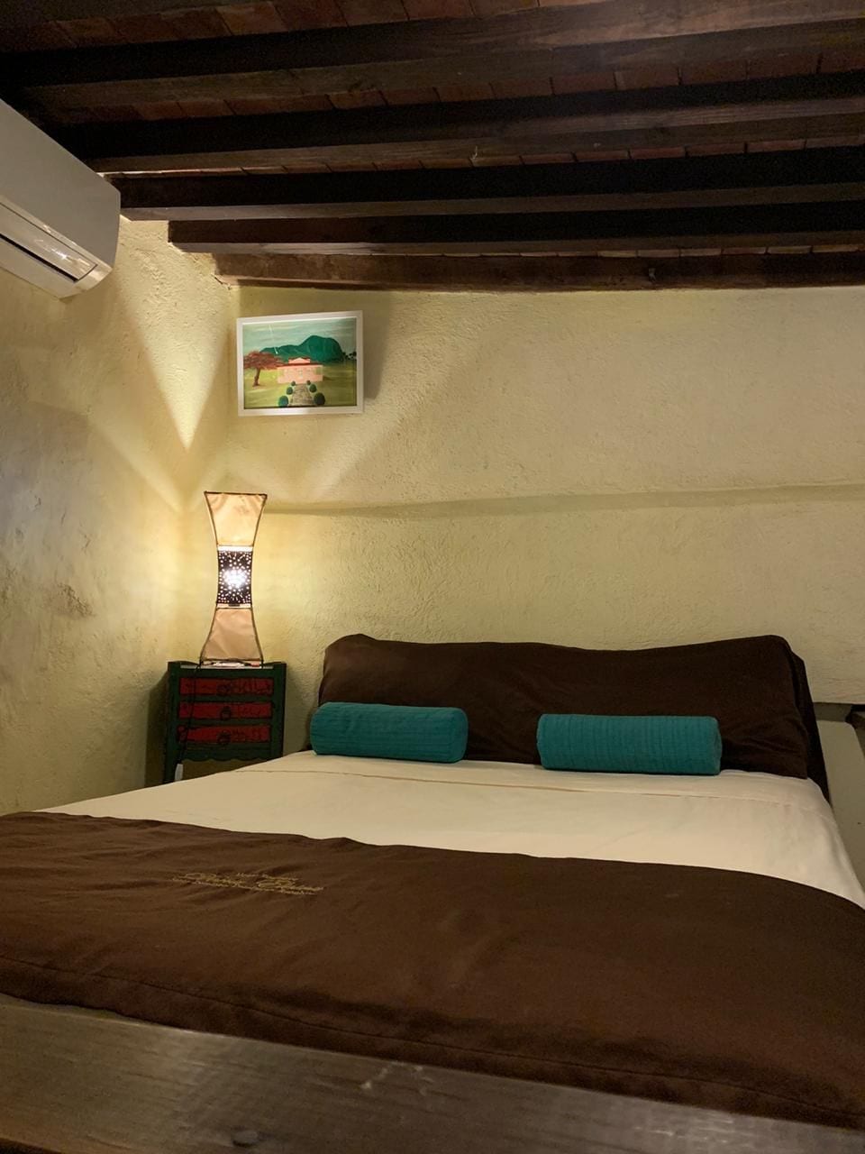 Un dormitorio con una cama, una mesita de noche, una lámpara y un cuadro en la pared.