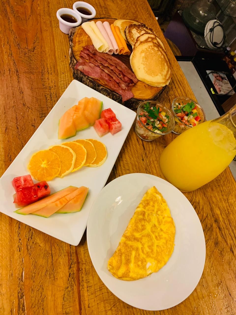 Une table de petit-déjeuner avec divers aliments, notamment des crêpes, du bacon, des œufs et des fruits frais.