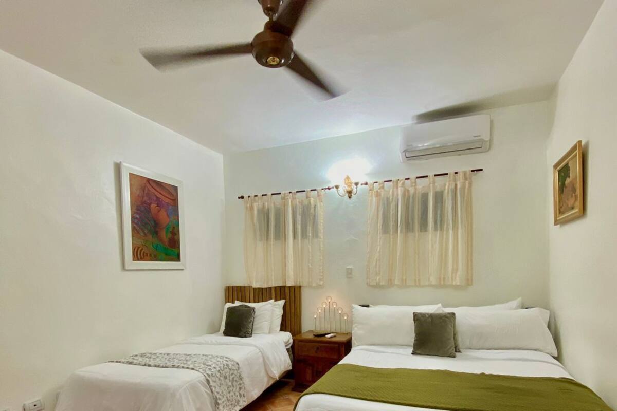 Ein Zimmer mit zwei Betten, einem Deckenventilator, einer Klimaanlage und einem Bild an der Wand.