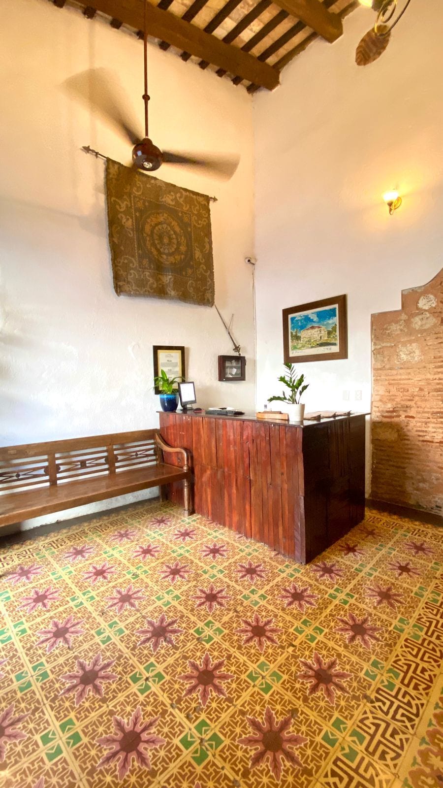 A room with a wooden bench, a reception desk, a patterned floor, a ceiling fan, and a wall-mounted light fixture.