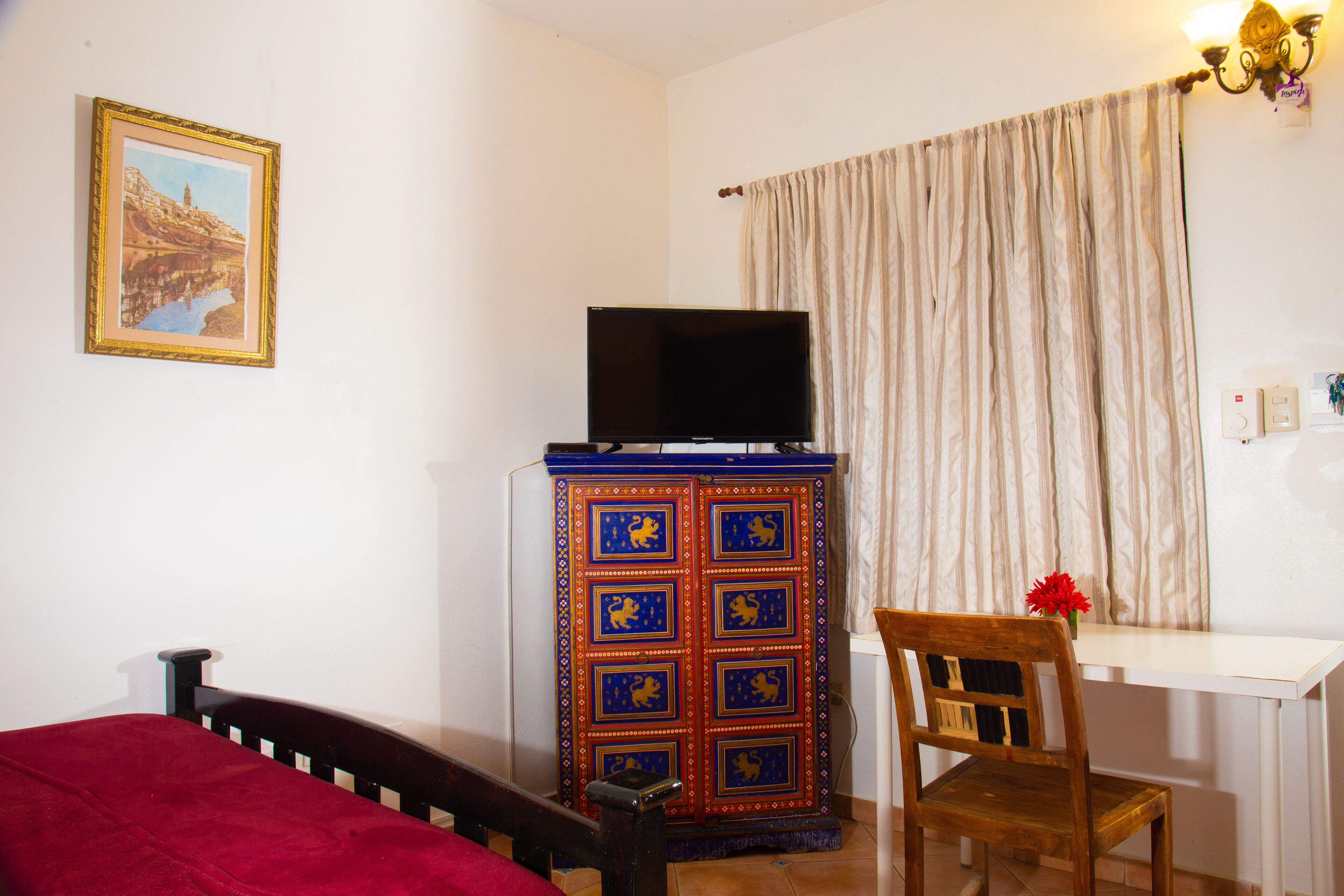 A room with a bed, a desk with a television, a chair, and a decorative cabinet.