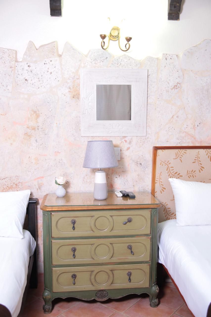 Une chambre avec deux lits, une table de chevet avec une lampe, un tableau encadré et un mur décoratif.