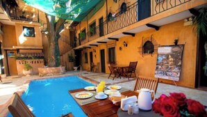 Un comedor junto a la piscina con una mesa dispuesta para el desayuno, rodeado de sillas y un banco de madera.