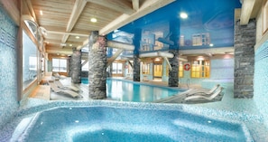 An indoor swimming pool with stone pillars, tiled walls, and lounge chairs.