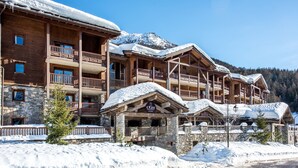 Una cabaña de madera de varios pisos con balcones y fachada de piedra, rodeada de montañas nevadas.