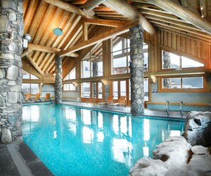 An indoor swimming pool with stone walls and wooden beams, large windows, and a view of the outside. - CGH Résidences & Spas L'Oree des Cimes (Landry)