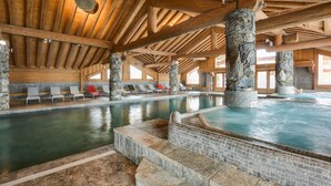 An indoor swimming pool with stone pillars, wooden beams, and lounge chairs.