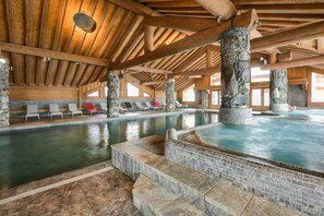 Una piscina interior con pilares de piedra, vigas de madera y sillones de descanso.