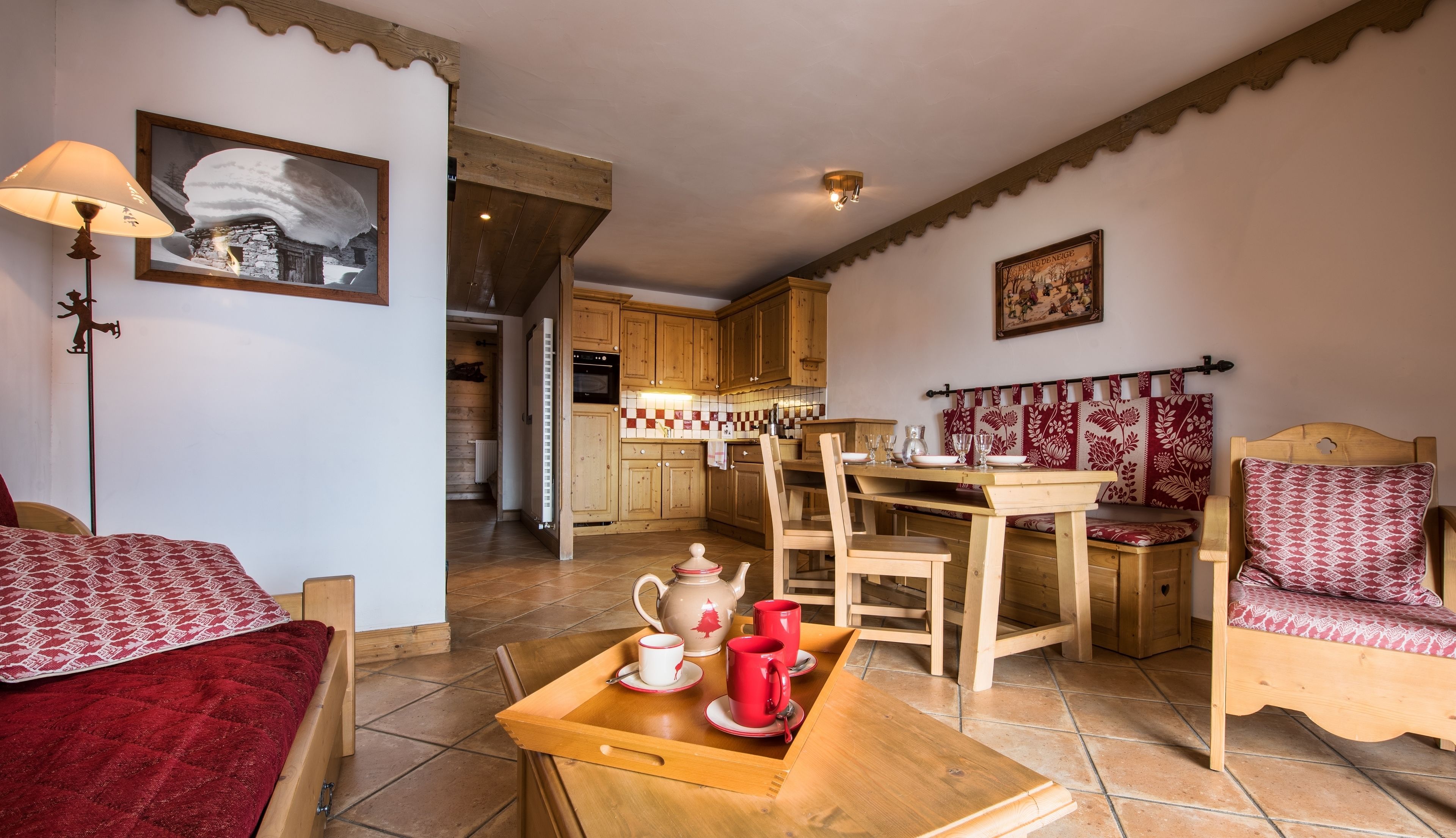 A cozy room with a wooden bed, a dining table with chairs, and a kitchen area in the background.